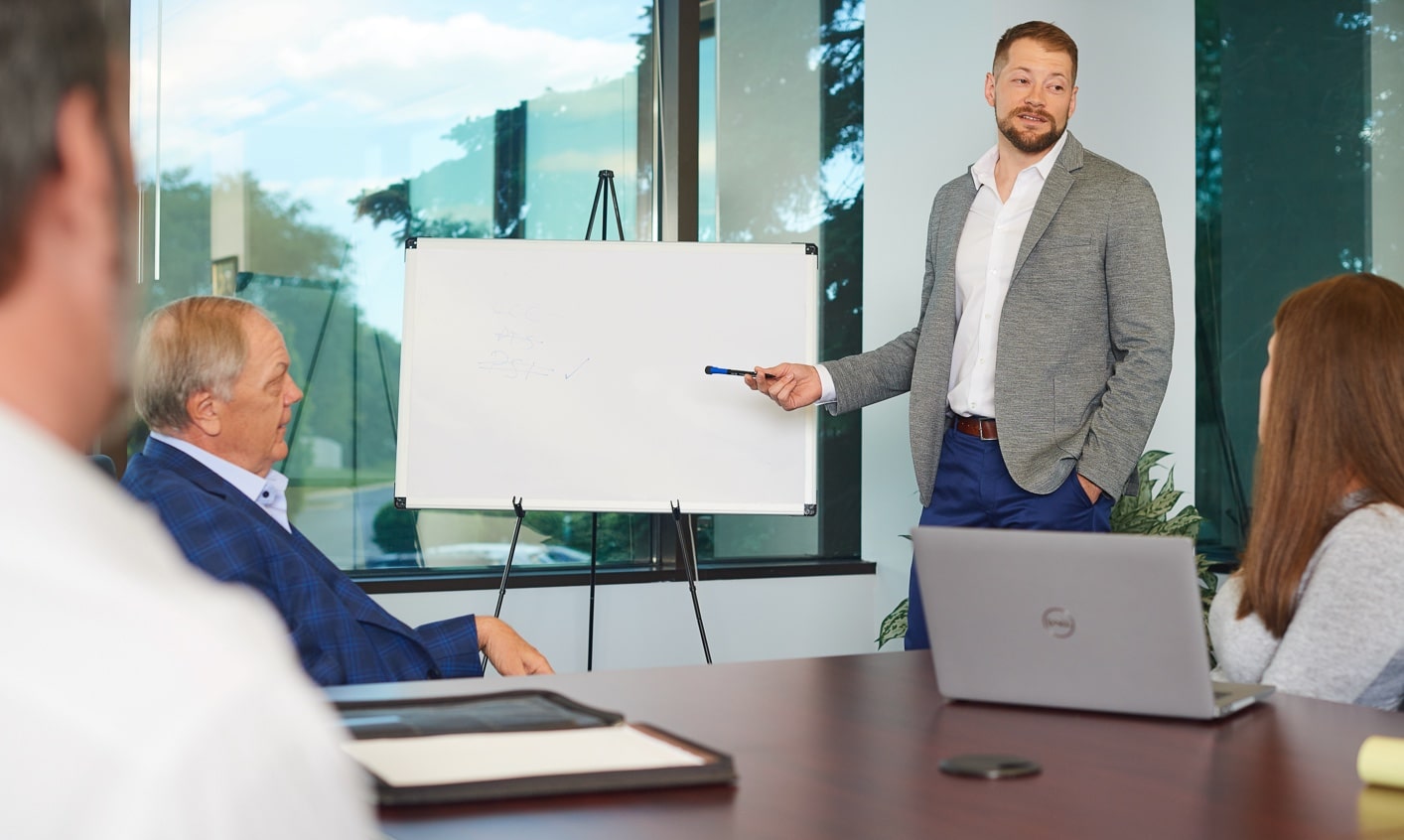 Young professional in business casual attire using a marker to point at whiteboard in boardroom