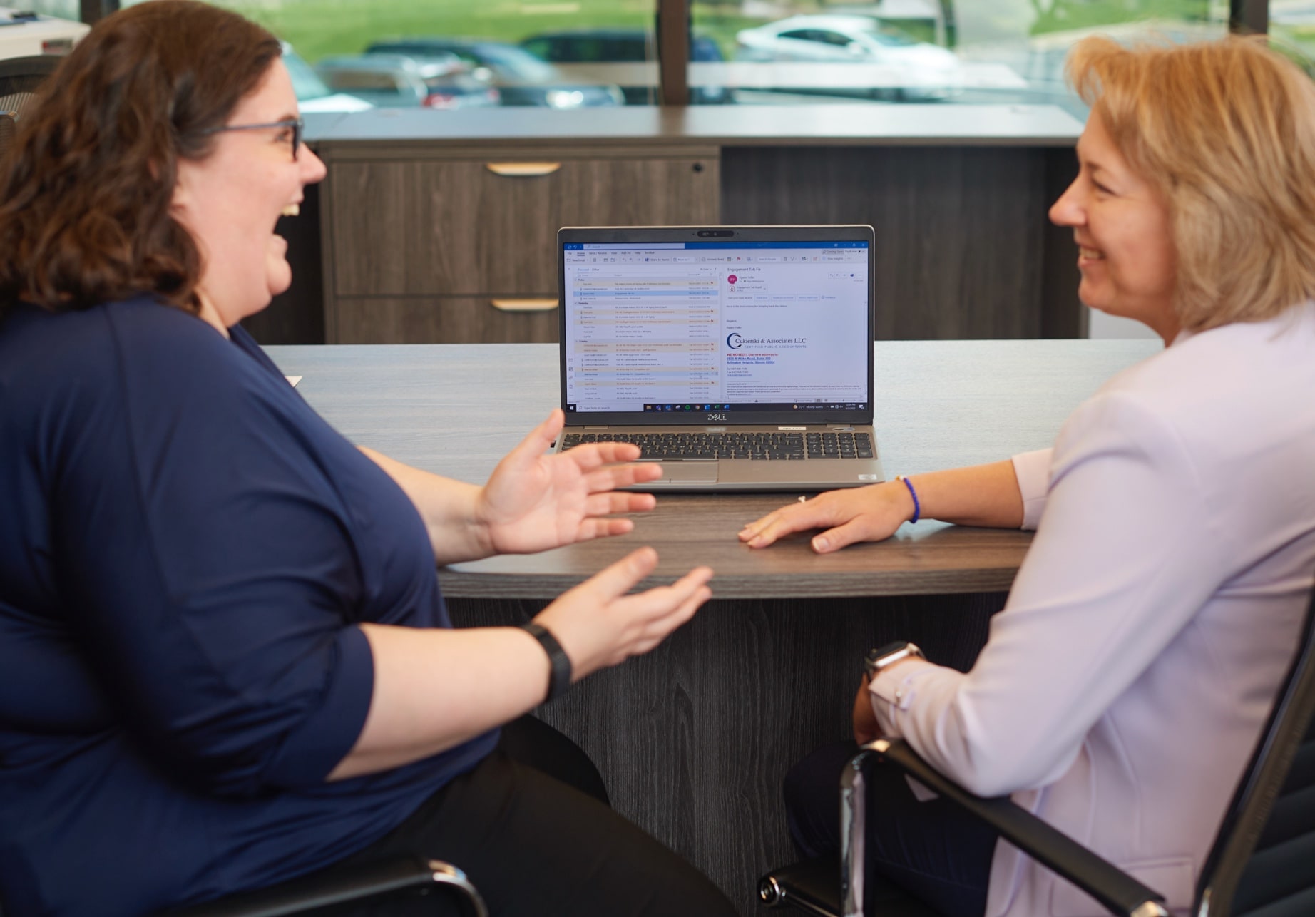 Two women sitting in office chairs having lively conversation in front of a laptop