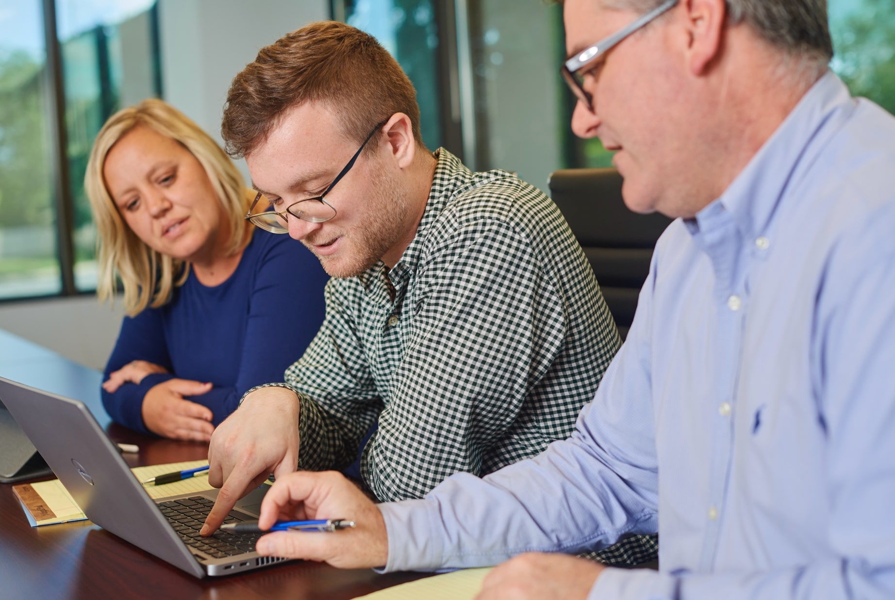 Two men and a woman looking at an open laptop