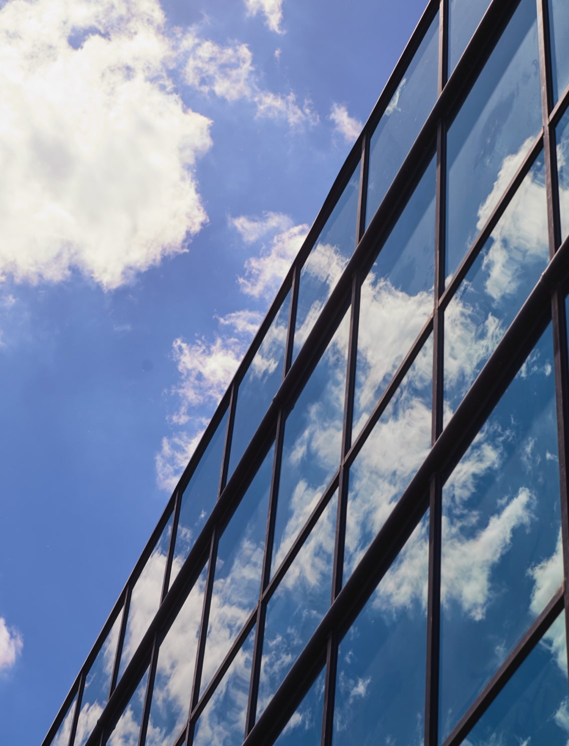 Exterior of glass-paned building reflecting a blue sky and clouds